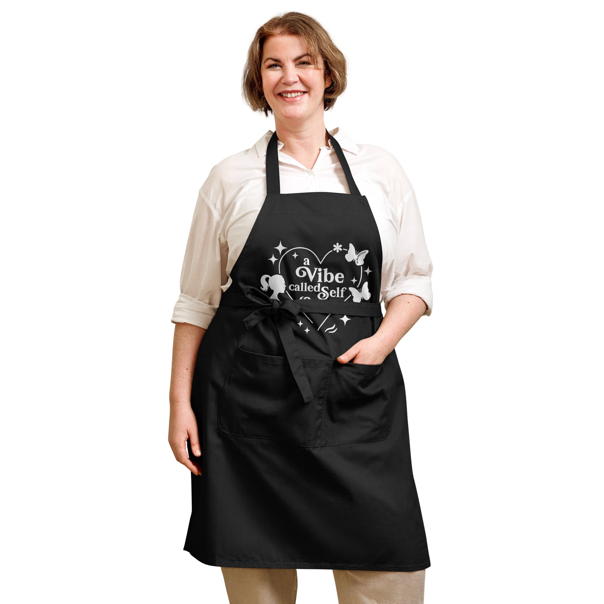 Woman smiling, wearing black apron, front view with self-love design, hand in pocket,stylish kitchen wear- SublimeElle Self - Love