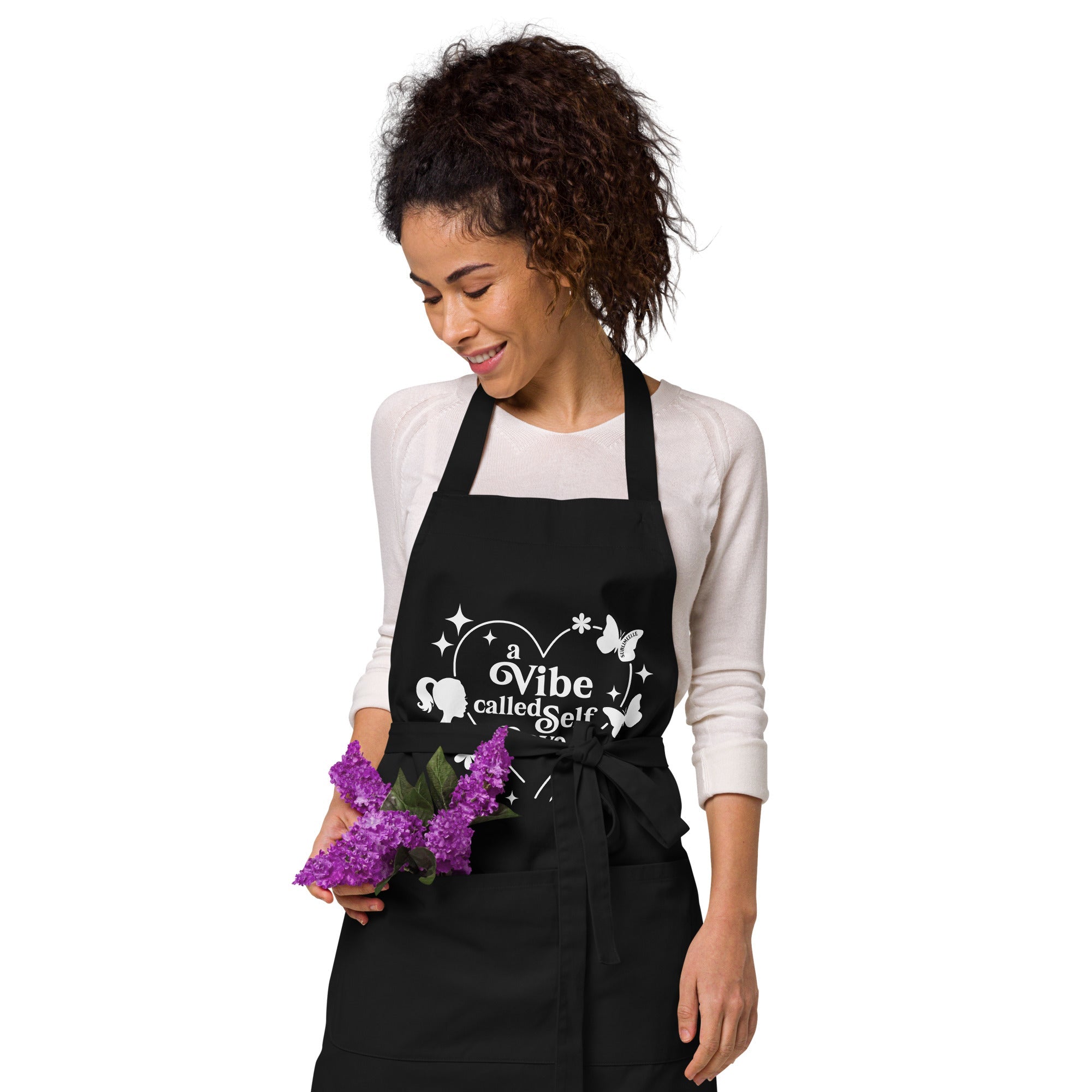 Woman wearing black apron with front pockets featuring flowers, showcasing self-love design, ideal for mindful cooking and self-care- SublimeElle Self - Love